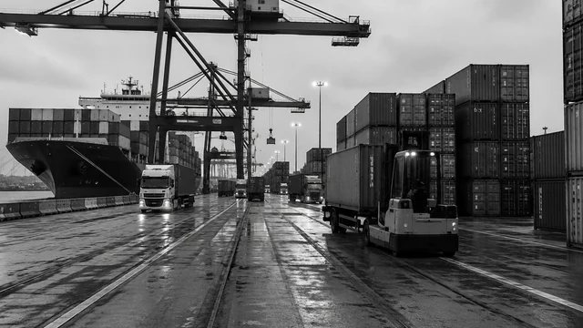 Containerterminal met portaalkranen, containerschip en vrachtwagens op een natte kade in de schemering