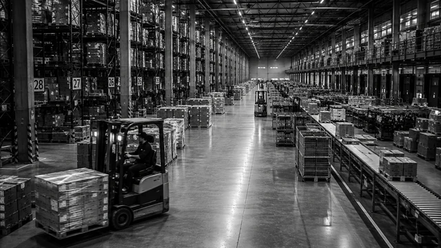 Groot modern distributiecentrum met hoge stellingen en heftrucks in een breed gangpad
