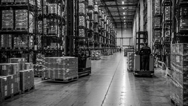 Vol magazijn met hoge stellingen tot aan het dak en een smal gangpad met orderverzameltrucks