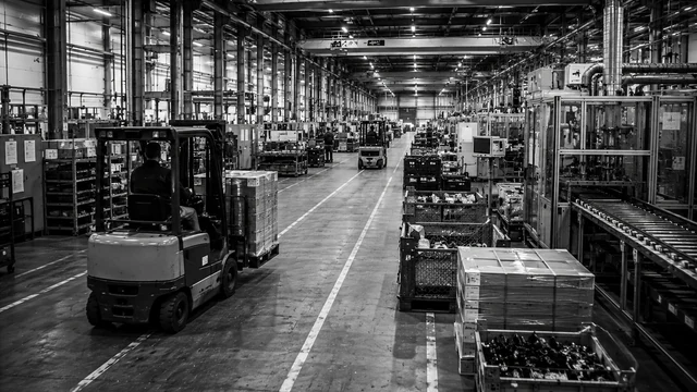 Productiehal met machines aan de ene zijde en heftrucks die materiaal aanvoeren door een breed middenpad